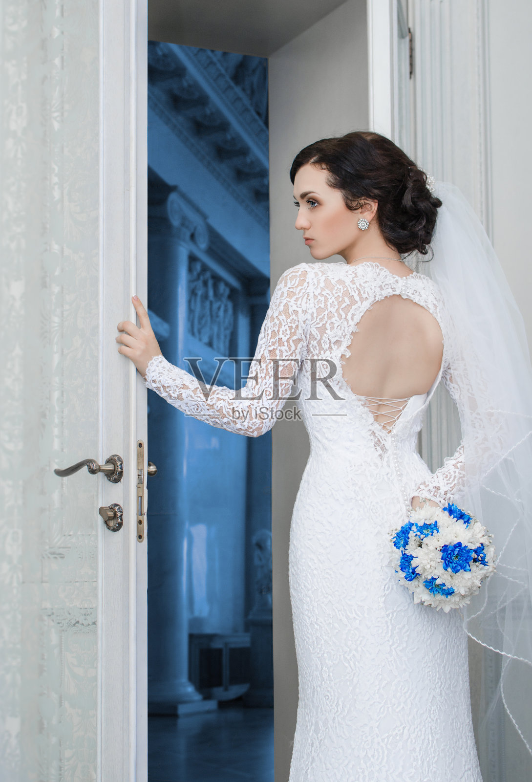 年轻的新娘捧着一束婚纱站在门口照片摄影图片