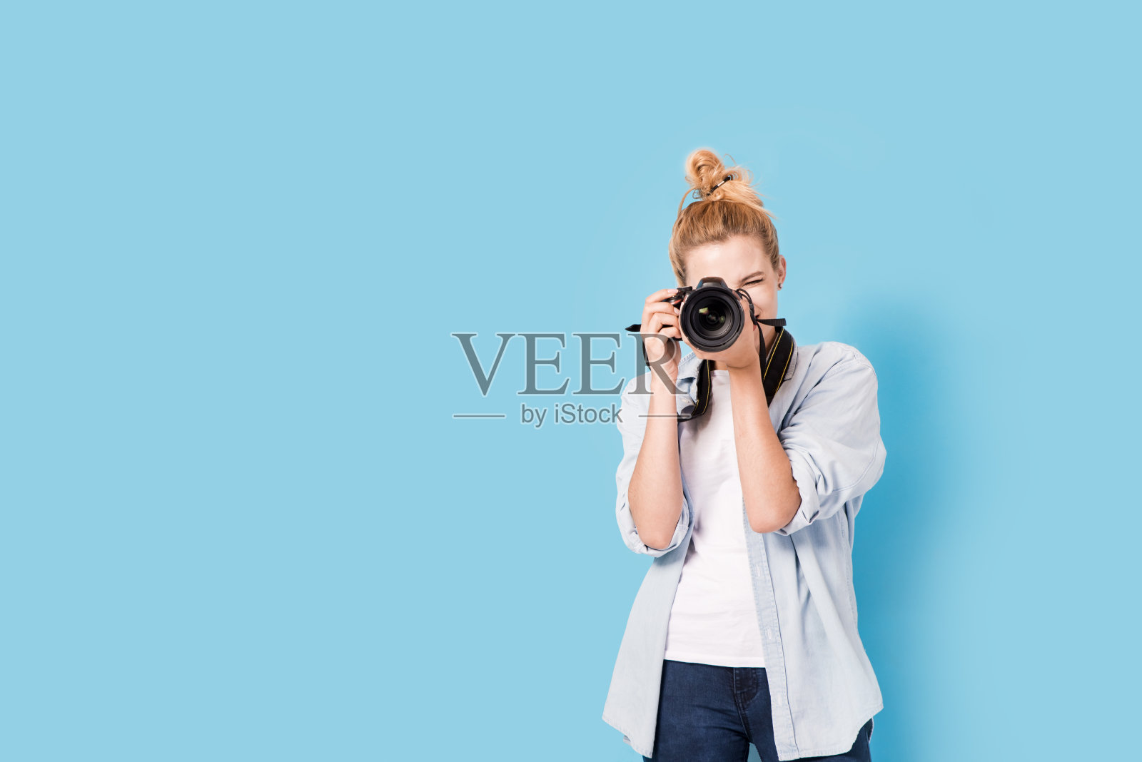 年轻的金发摄影师正在拍照。模型孤立的蓝色背景与复制空间照片摄影图片
