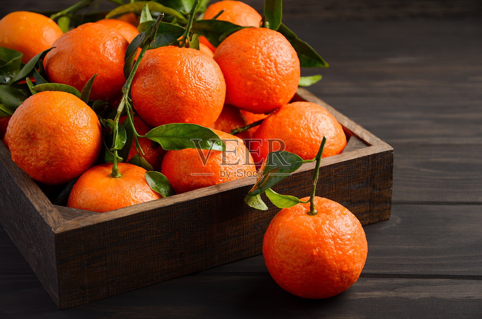 鲜橘小柑橘，叶子在深色木质背景上照片摄影图片