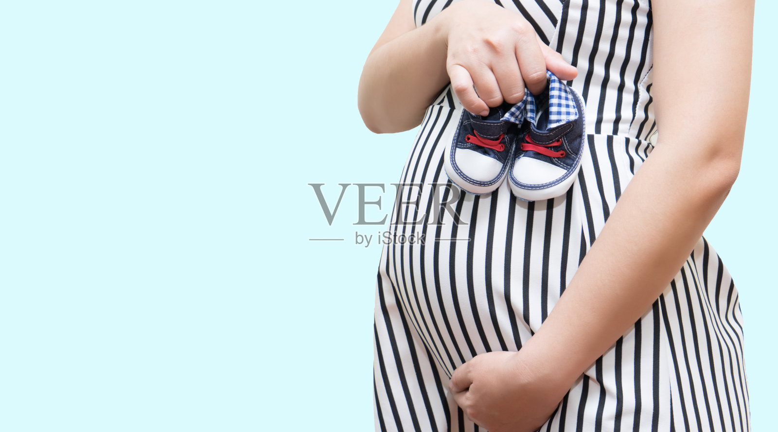 孕妇抱着婴儿的鞋子在白色的背景上照片摄影图片