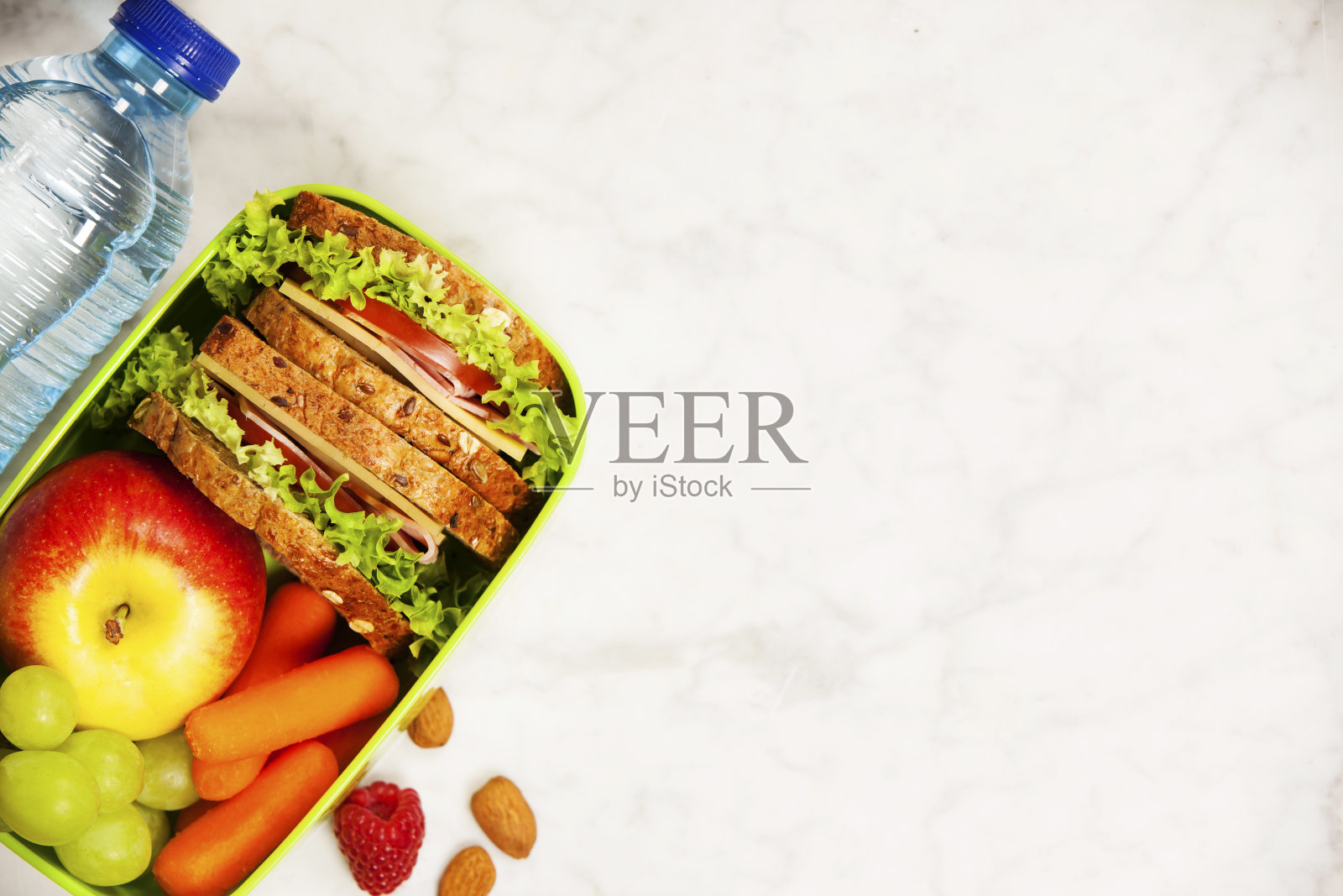绿色的学校午餐盒，有三明治，苹果，葡萄，胡萝卜和一瓶水照片摄影图片