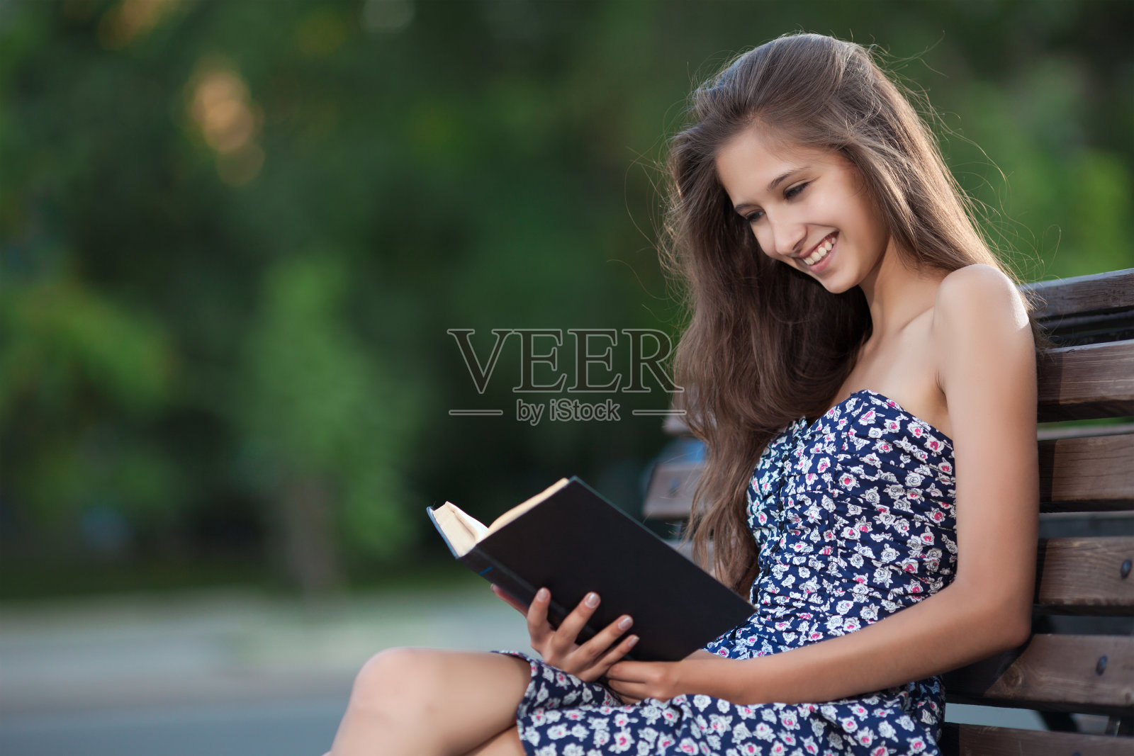 漂亮的黑发女人坐在长凳上看书照片摄影图片