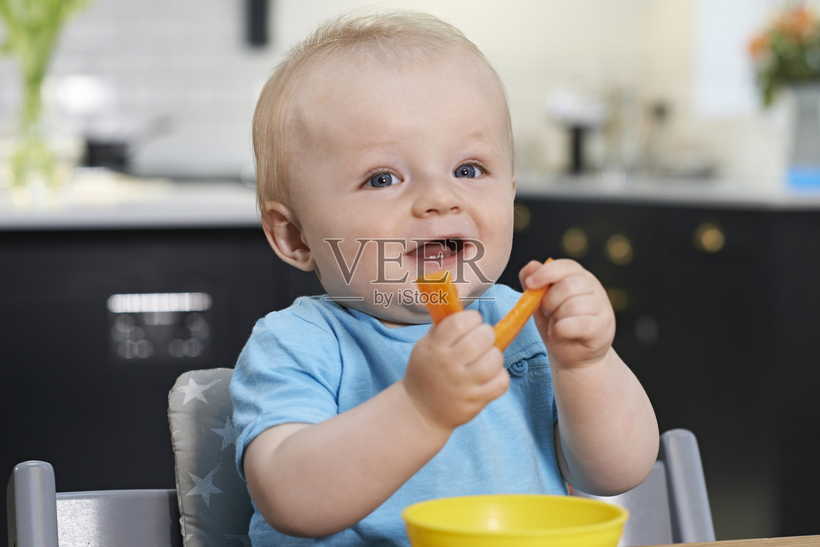 快乐的幼童坐在桌前吃新鲜的胡萝卜照片摄影图片