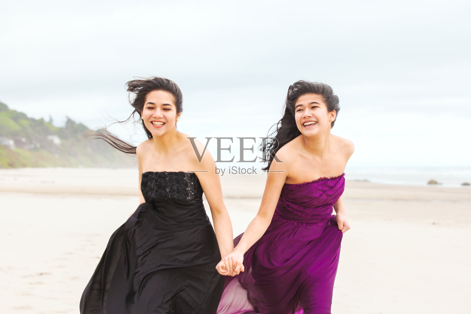 两个十几岁的女孩在凉爽的阴天在海滩上跑步照片摄影图片