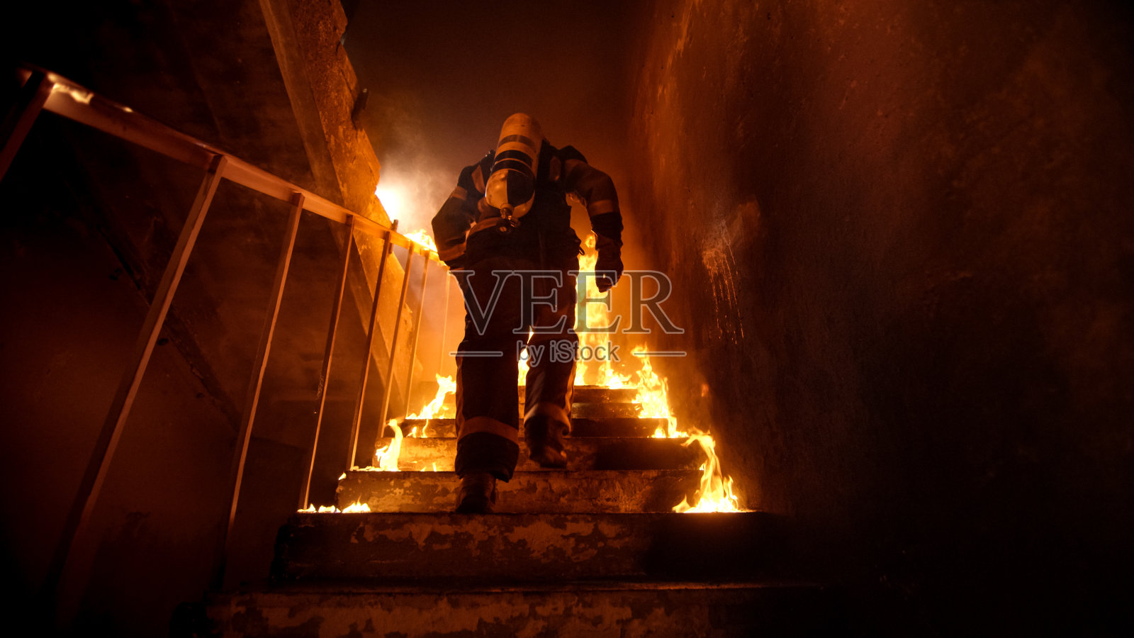 强壮和勇敢的消防员在燃烧的建筑物上楼梯。楼梯被明火燃烧。照片摄影图片