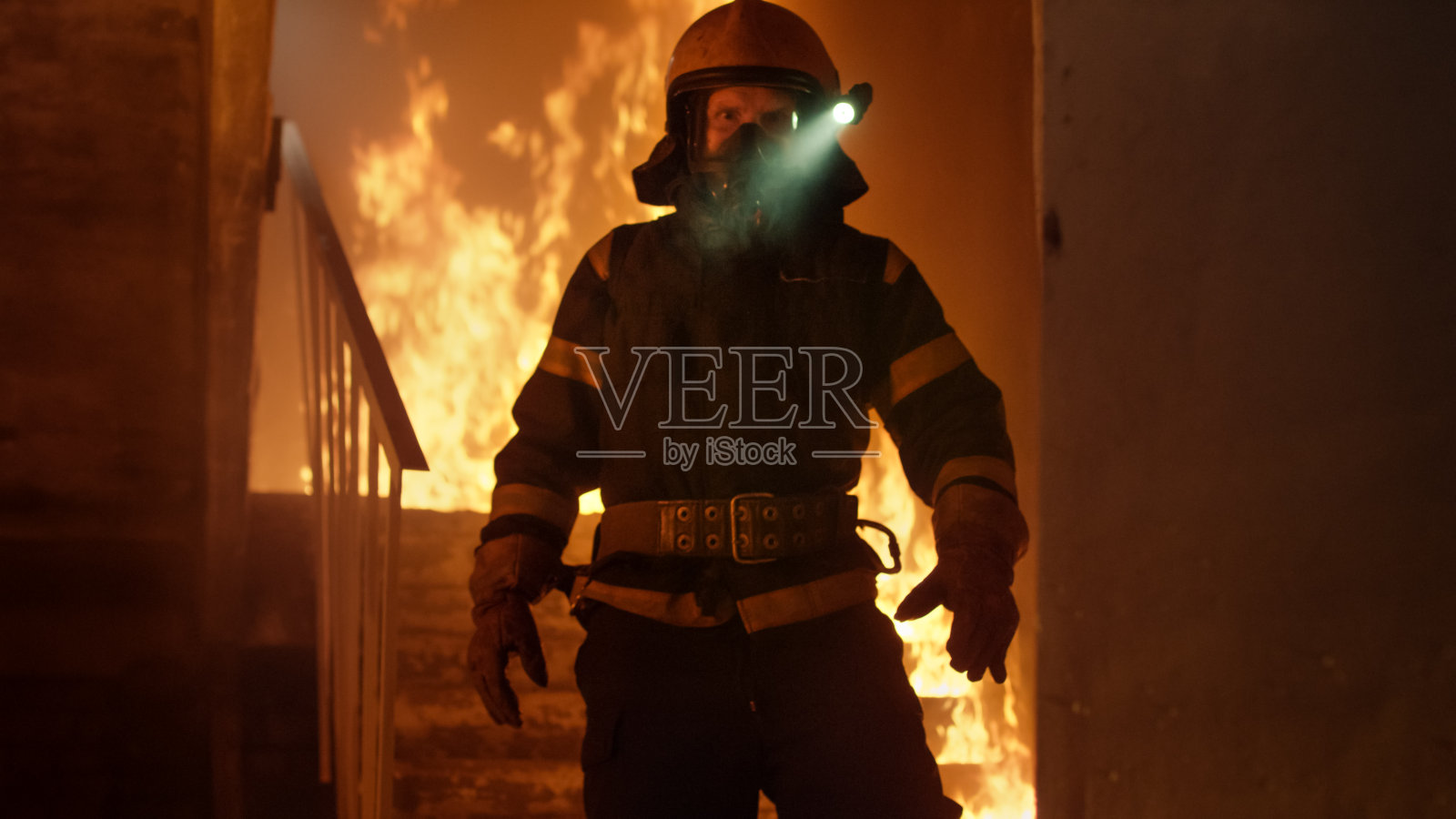 勇敢的消防员打开头盔上的手电筒，独自站在燃烧的楼梯上。在背景中开火。照片摄影图片