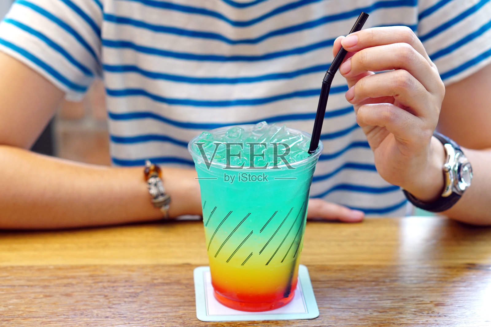 彩色鸡尾酒或热带鸡尾酒-塑料杯的能量饮料，柠檬水，橙汁和西瓜糖浆放在木桌上。照片摄影图片