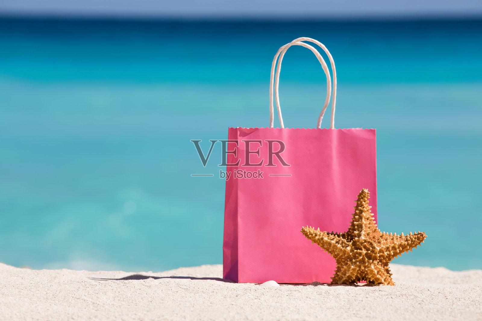 购物袋和海星在沙滩上对抗绿松石加勒比海水照片摄影图片