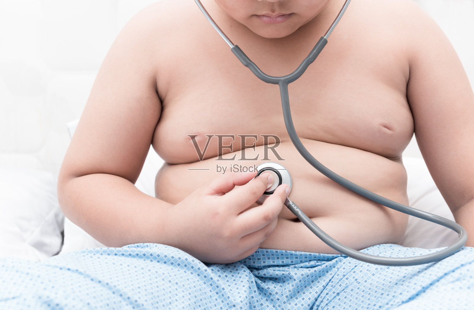 胖男孩用听诊器检查胃。照片摄影图片