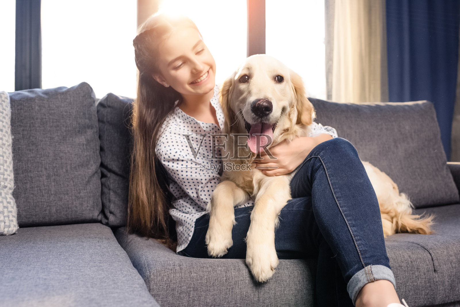 十几岁的女孩在家里的沙发上拥抱金毛猎犬照片摄影图片