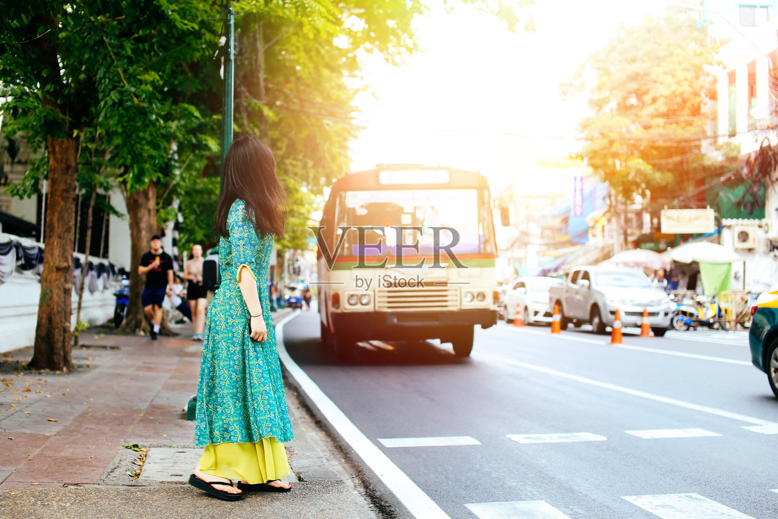 泰国曼谷，身着亚洲传统服饰的女子站在道路上挥手示意出租车或公交车等交通服务照片摄影图片