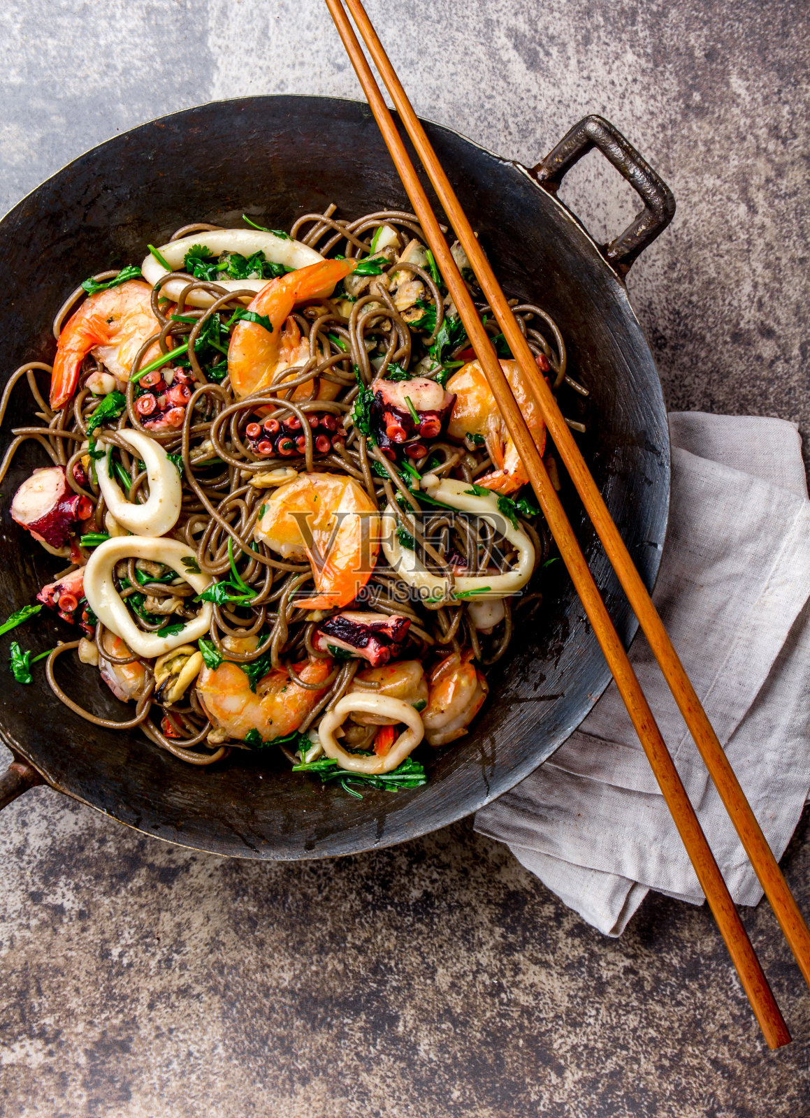 荞麦炒面海鲜-虾，章鱼，鱿鱼在铸铁亚洲炒锅与烹饪筷子。俯视图，石头背景照片摄影图片