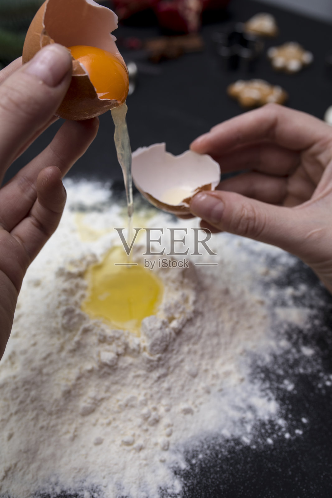 女性面包师的手打碎鸡蛋成生面团的特写。烘焙和食品准备的概念。照片摄影图片
