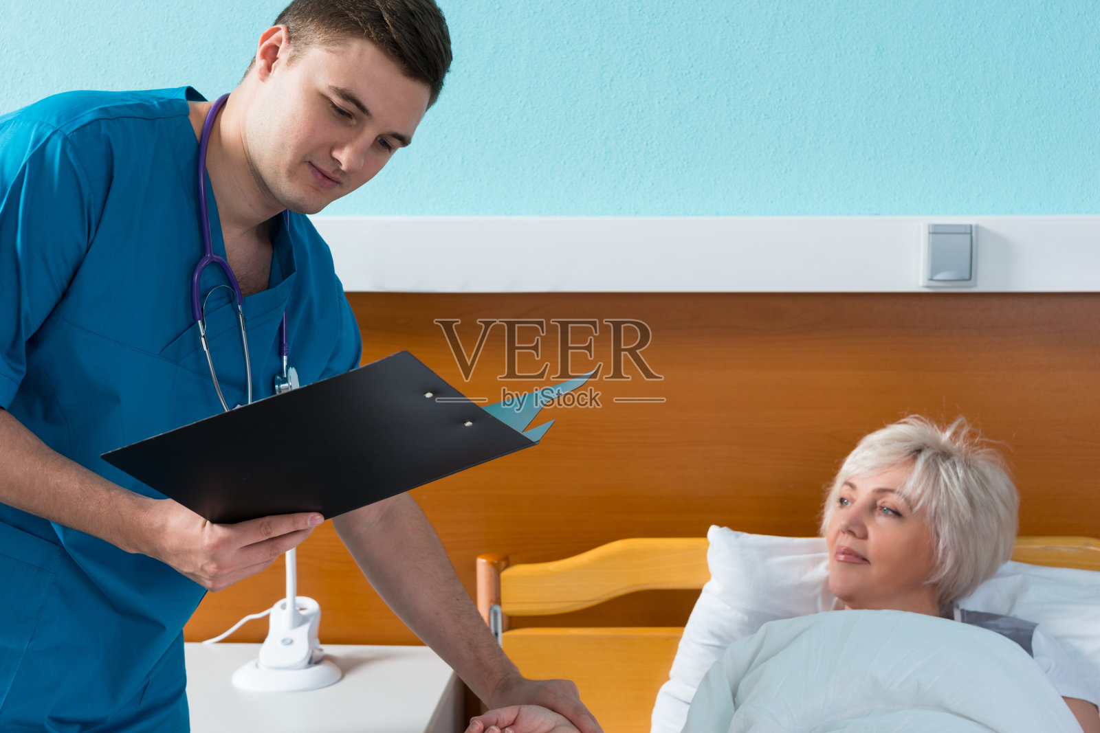 年轻的男医生穿着制服，脖子上挂着声音内窥镜，正在给他的女病人测量脉搏照片摄影图片