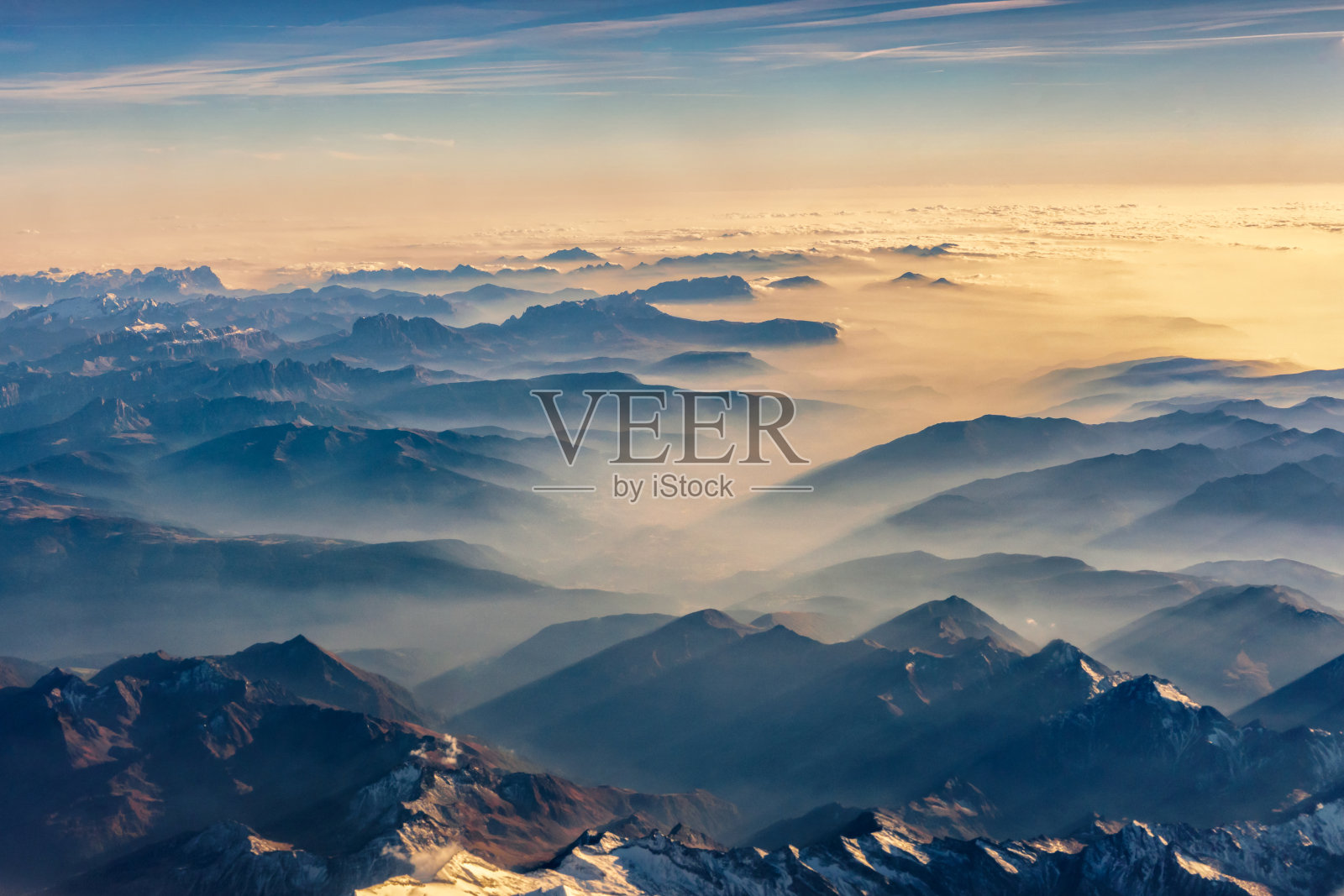 从飞机上俯瞰，透过云层从山顶俯瞰美丽的山景。照片摄影图片