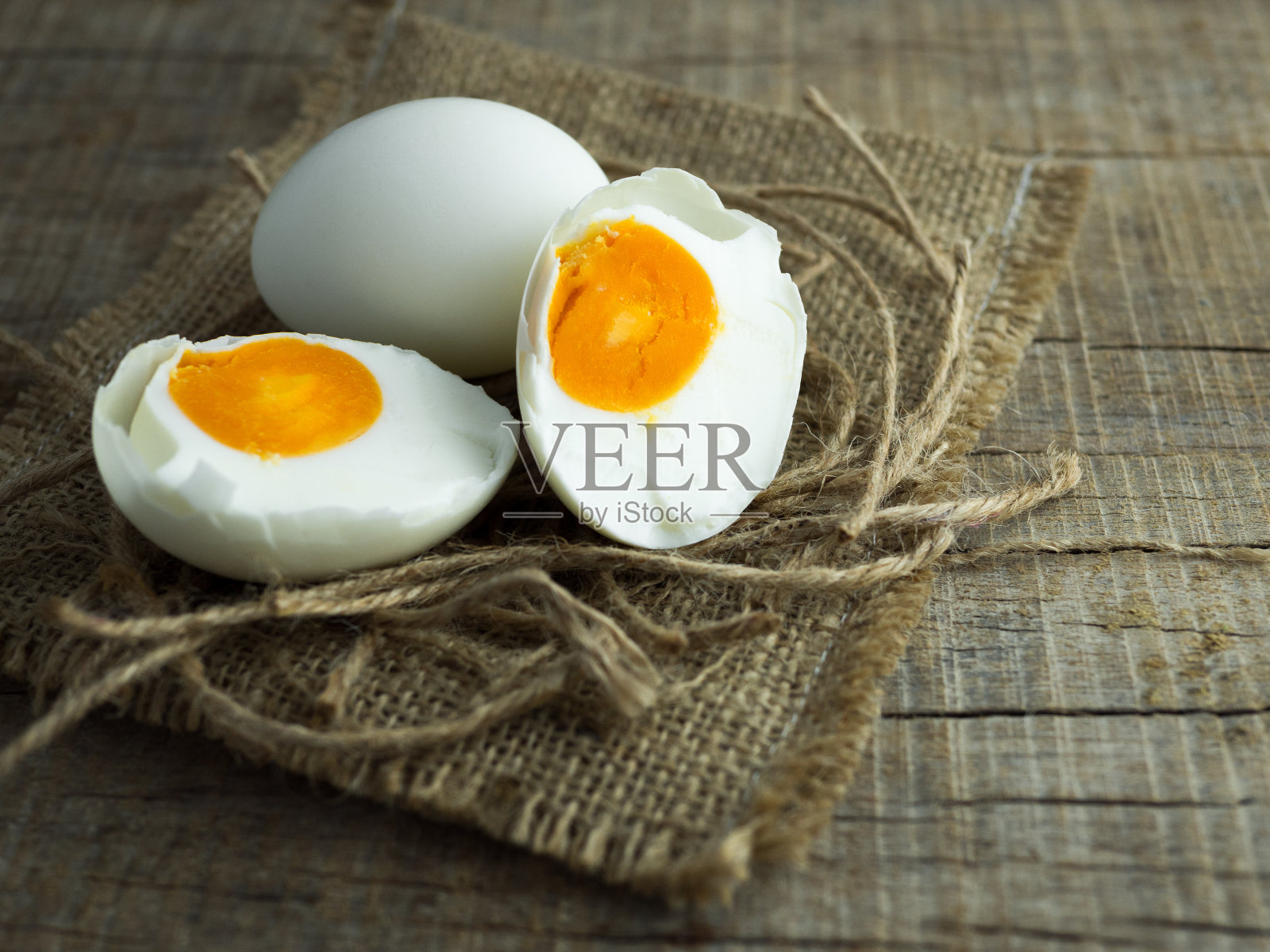 鸭蛋，白蛋，咸蛋和蛋黄在旧麻袋和绳子与木制背景。照片摄影图片
