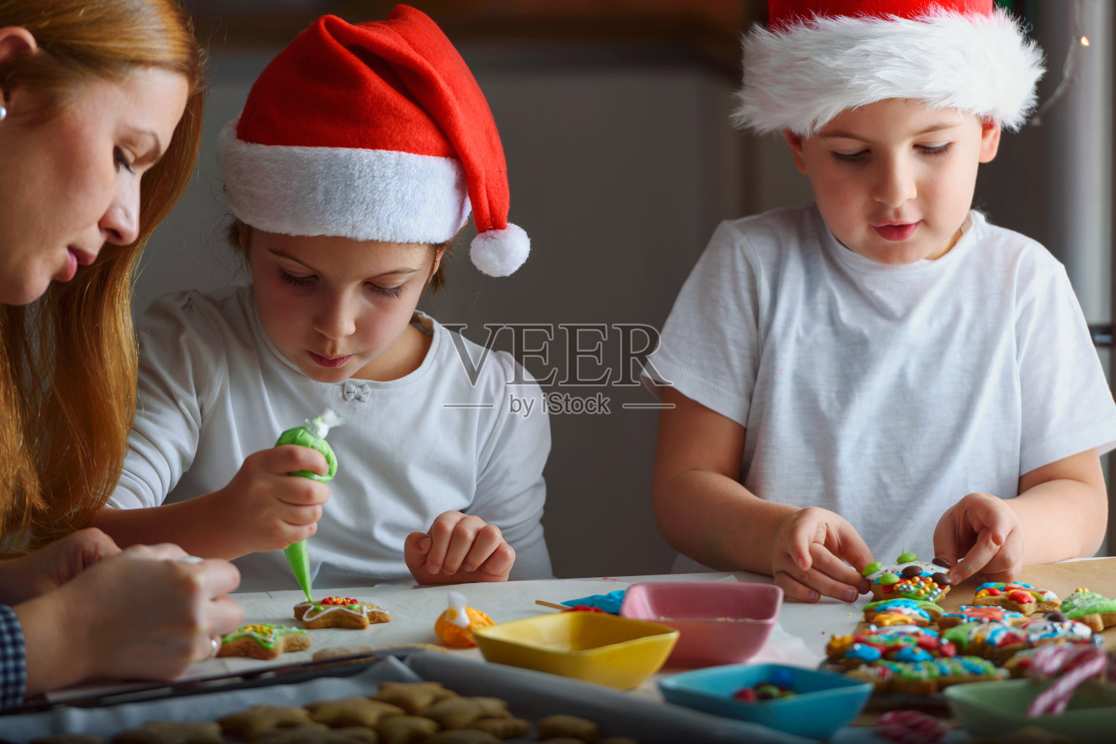 母亲和两个快乐的孩子在家里装饰节日饼干照片摄影图片