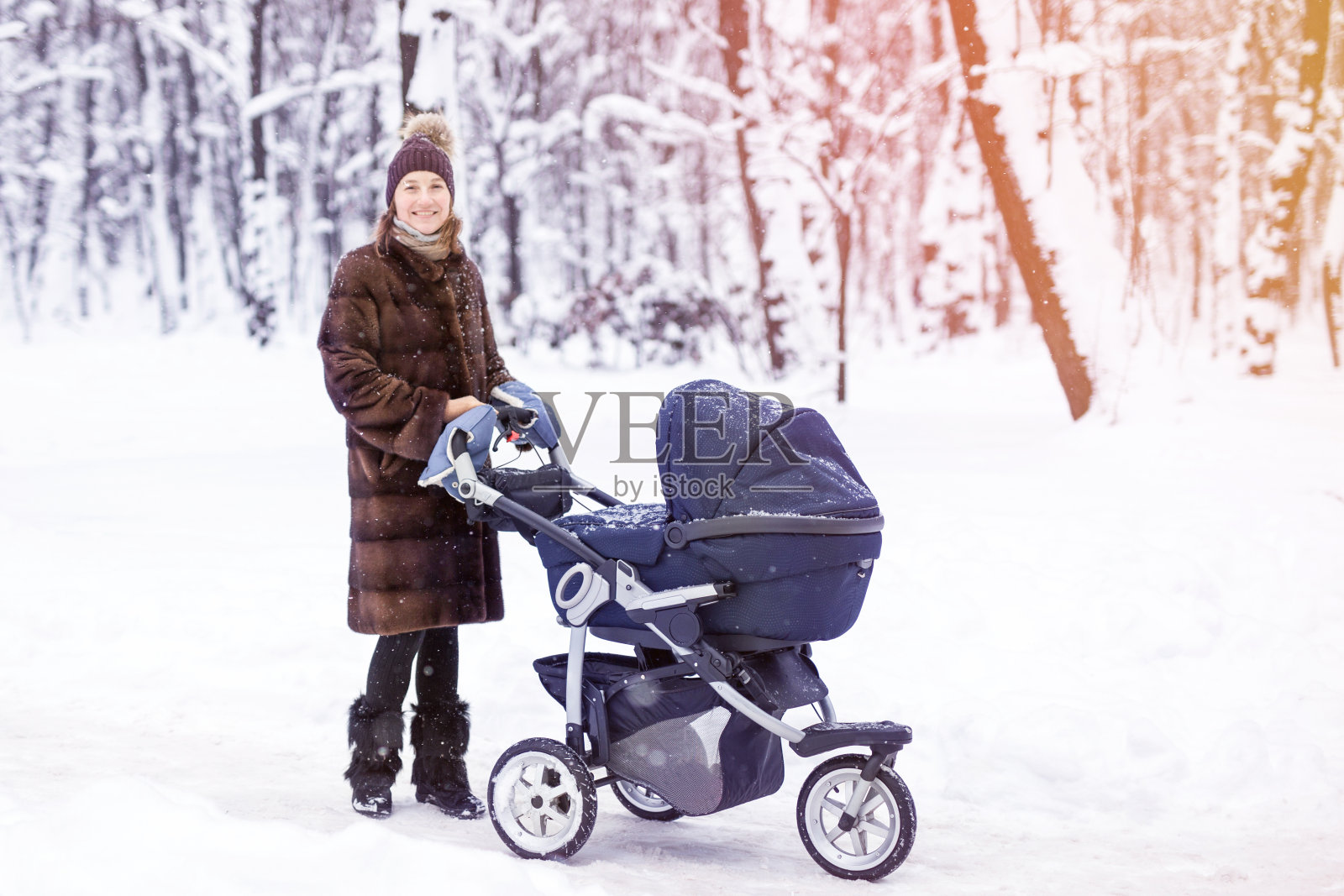 一个女人在冬天的森林里推着婴儿车。照片摄影图片