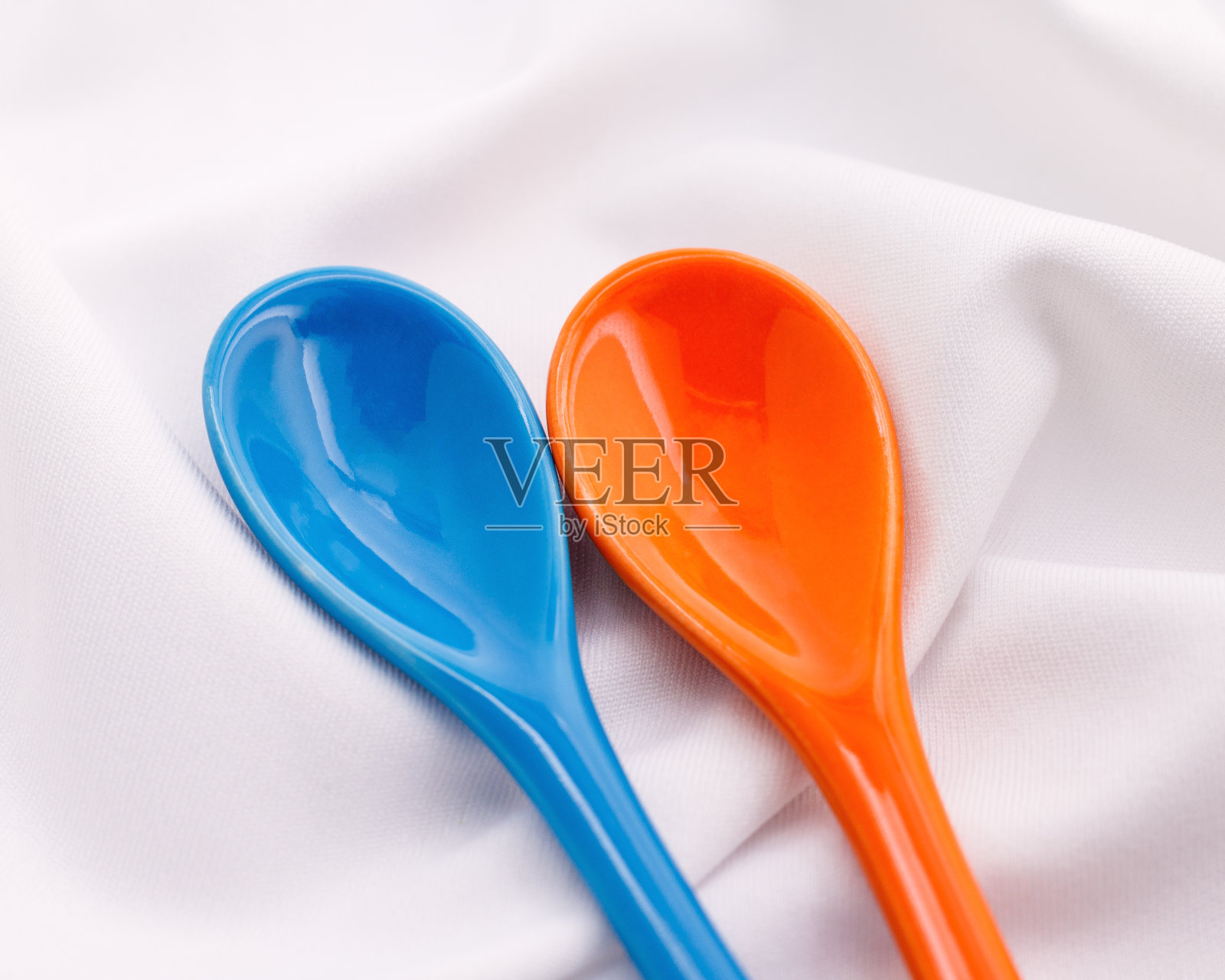 白色织物背景上的蓝色和橙色陶瓷勺。色彩斑斓的概念。照片摄影图片