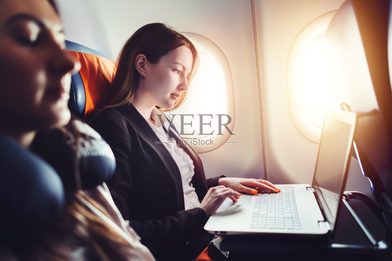 在飞机上靠窗坐着用笔记本电脑工作的女企业家照片摄影图片