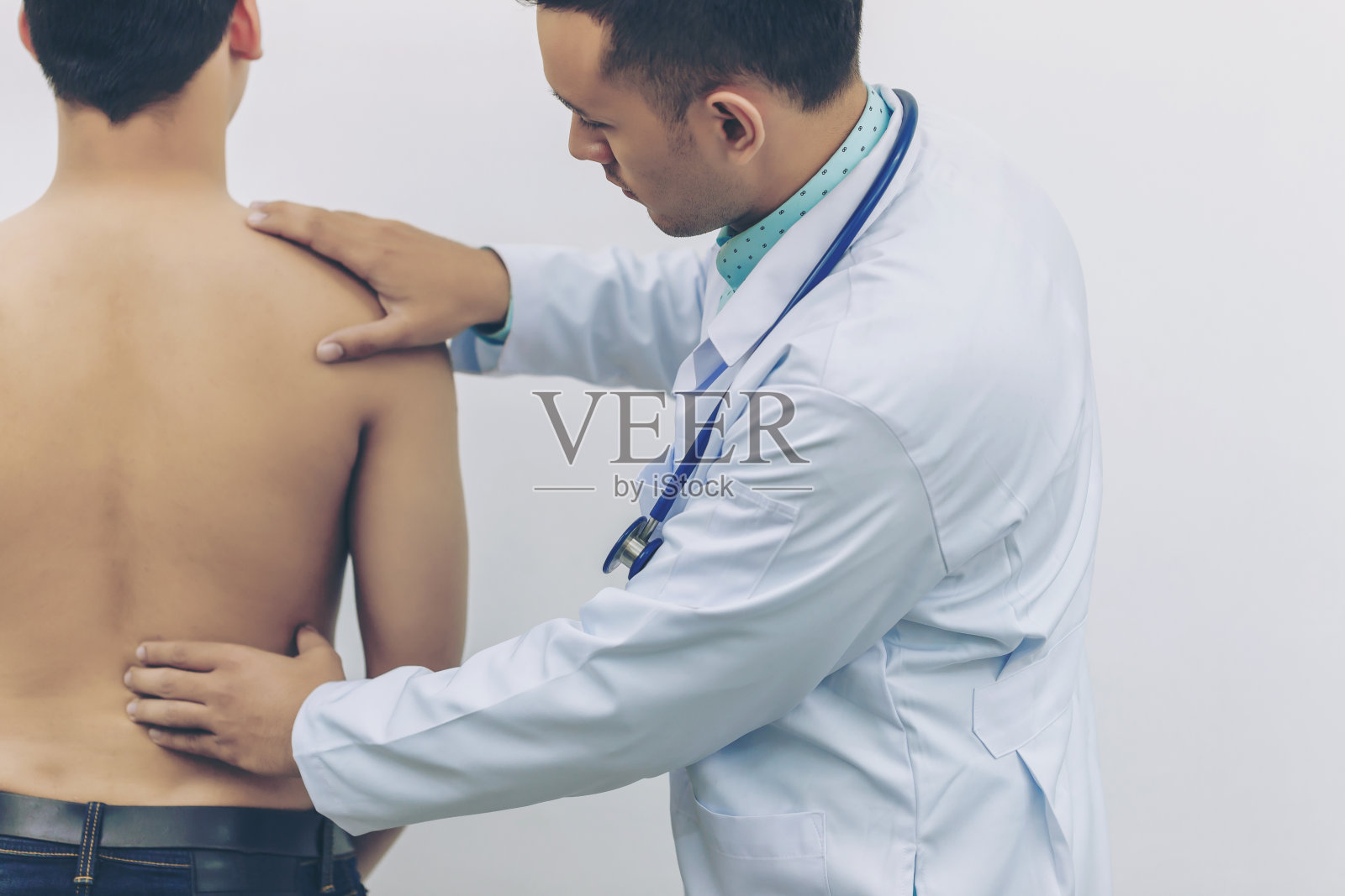 医生在医院用听诊器触摸背部钢板，以确定背部疼痛的原因。体检的概念，医疗保健。照片摄影图片