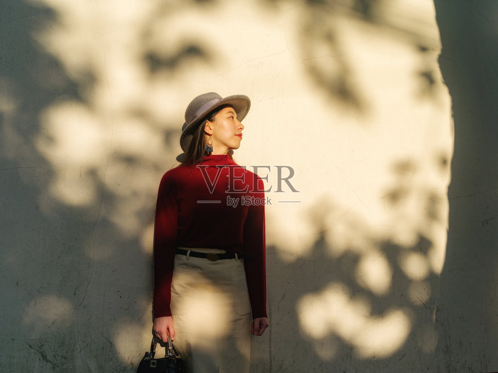 美丽的中国年轻女子站在温暖的阳光下，墙上有阴影。照片摄影图片