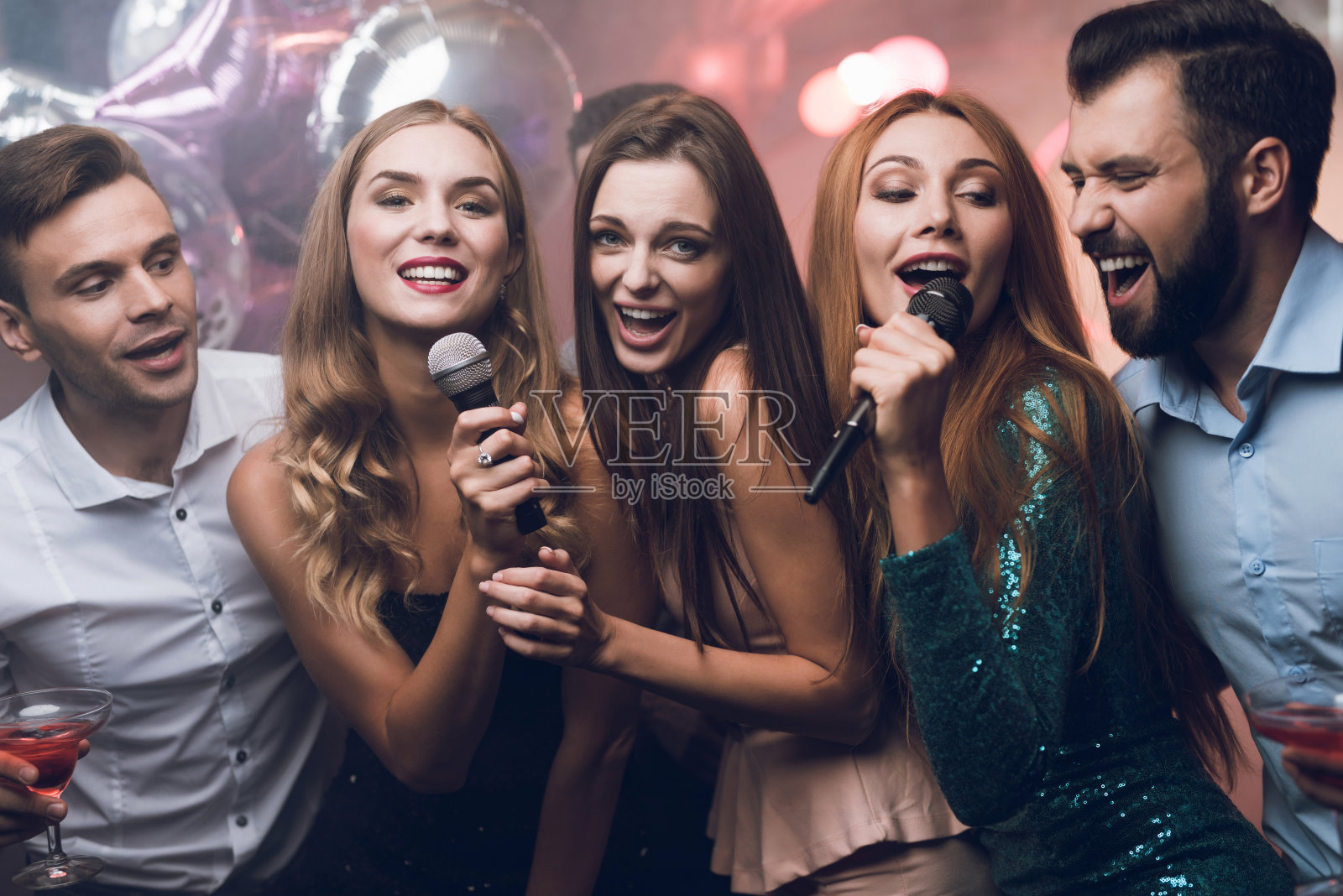 三个漂亮的女孩在卡拉ok俱乐部唱歌。他们后面的人在等着轮到他们。照片摄影图片