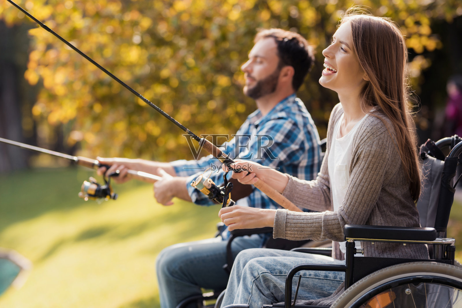 一个女人和一个坐在轮椅上的男人坐在湖边。他们手里拿着纺纱机，正在钓鱼。照片摄影图片