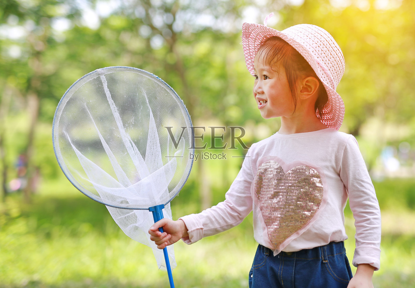 可爱的亚洲小女孩戴着草帽和蚊帐在田野里玩夏天。照片摄影图片