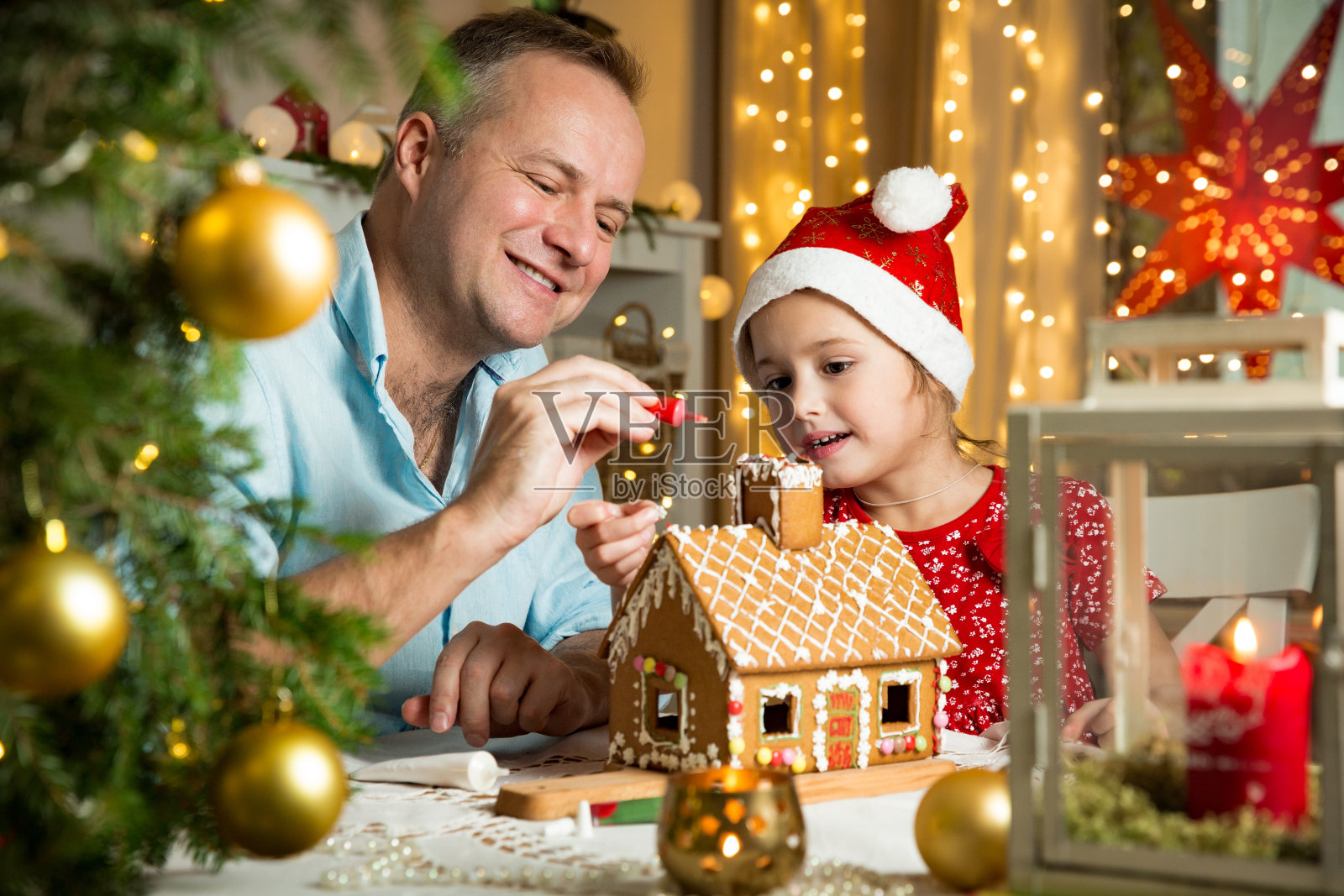 父亲和可爱的女儿在红帽子建筑圣诞姜饼屋照片摄影图片