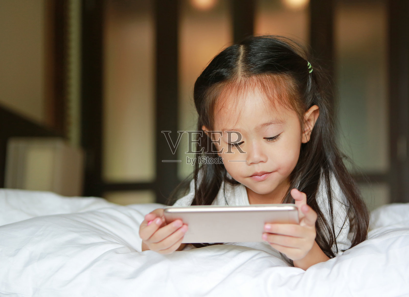 亚洲小女孩在床上看智能手机。孩子的发展。照片摄影图片