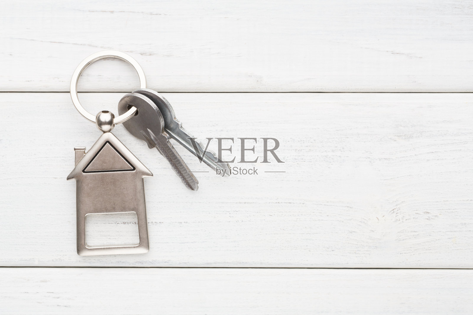 一串钥匙和房子形状的钥匙链在白色木头上照片摄影图片