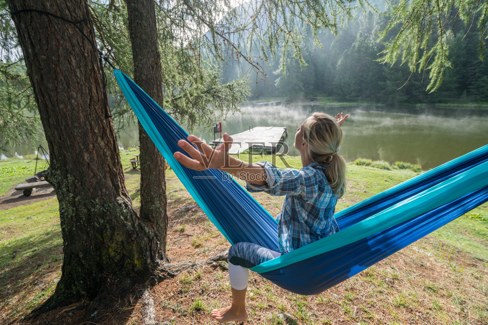 年轻女子躺在湖边的吊床上，双臂张开照片摄影图片