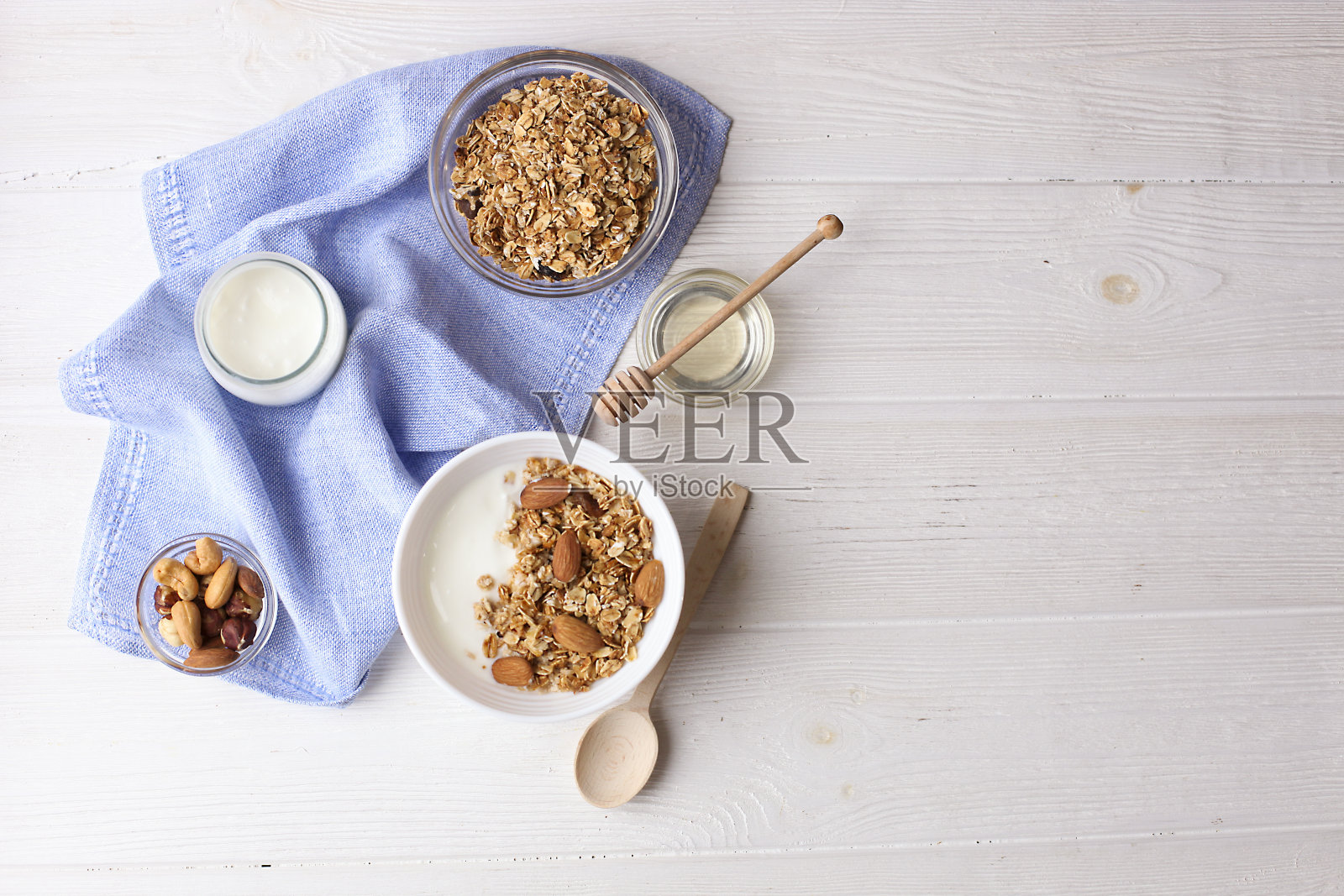 格兰诺拉麦片是一种超级食物，有杏仁，腰果，干果，葡萄干，陶瓷碗里的樱桃，牛奶和希腊酸奶放在白色的木桌上，俯视图照片摄影图片