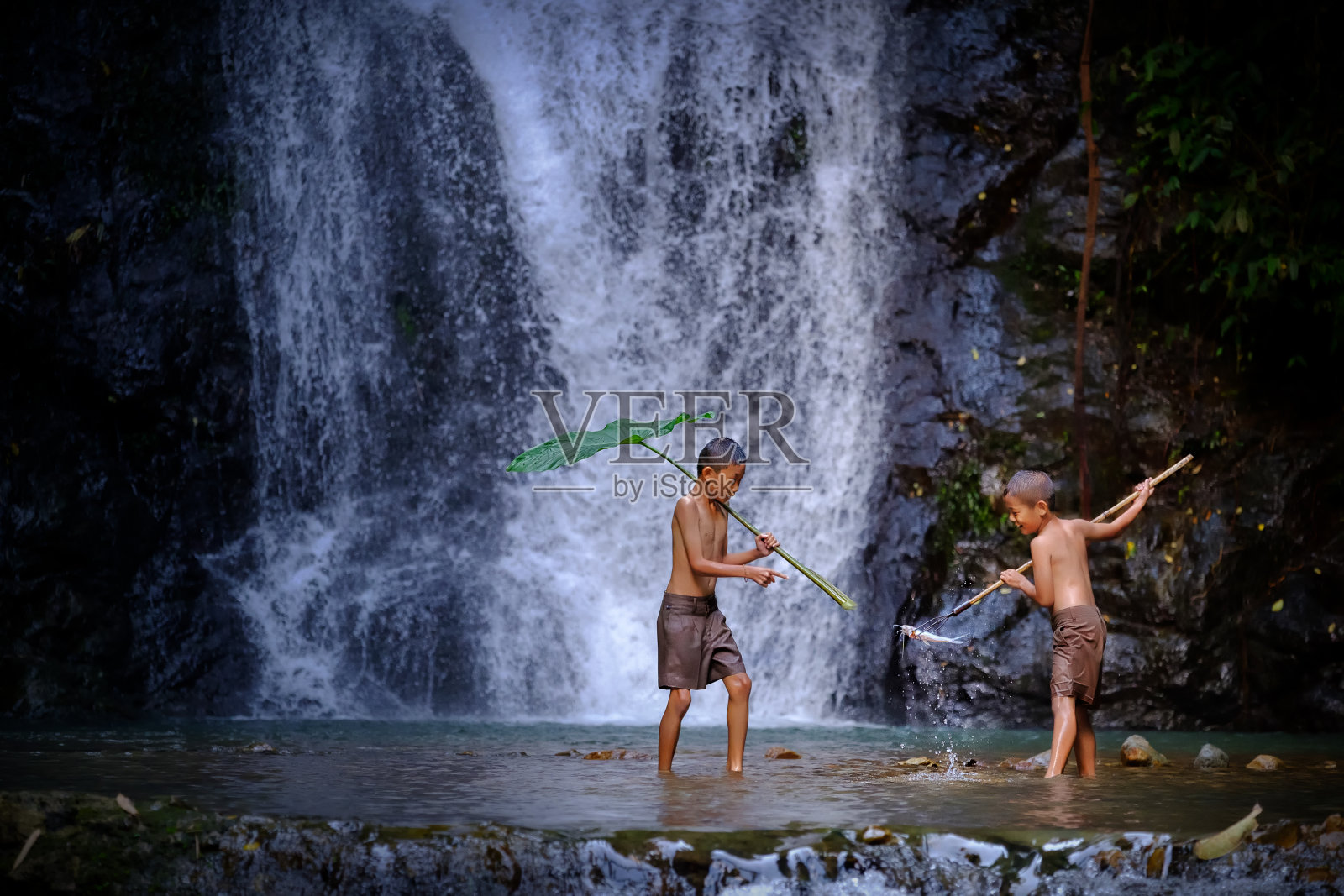 两个男孩笑着在泰国乡下的瀑布钓鱼。钓鱼男孩亚洲由鱼钩在小溪与美丽的背景照片摄影图片