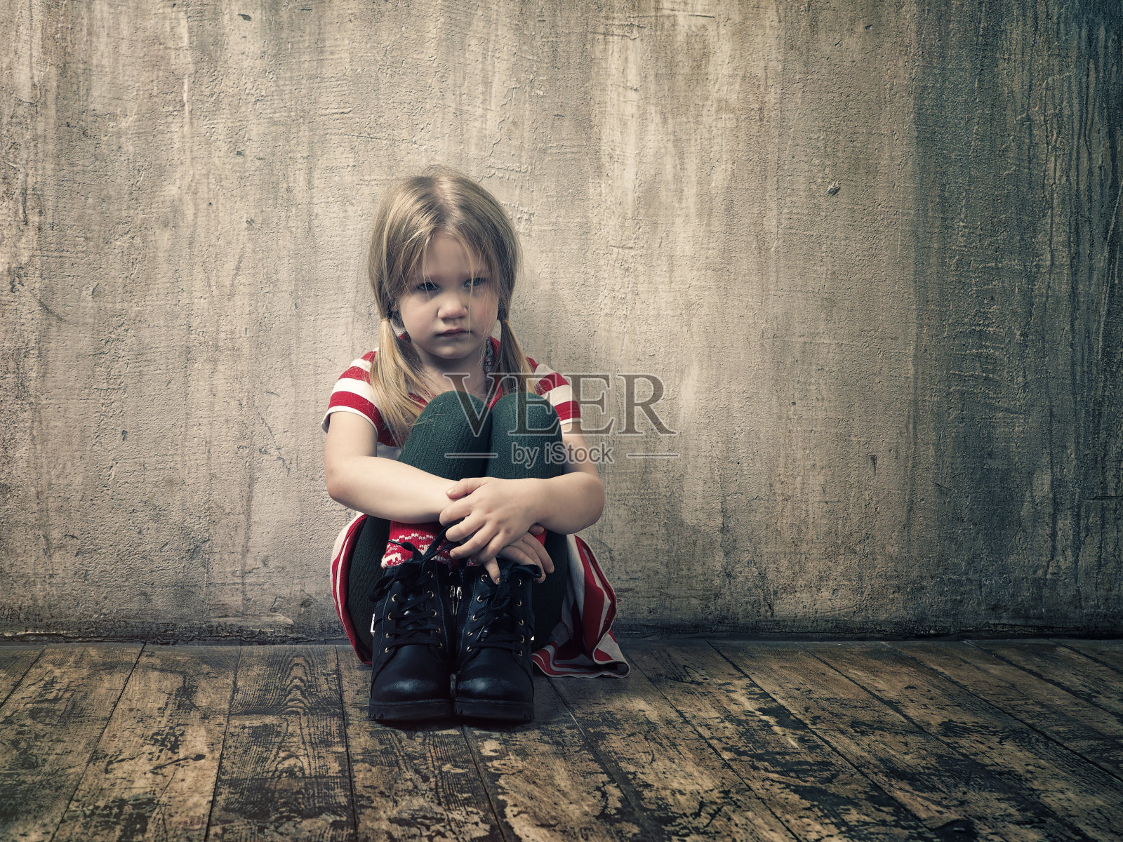 悲伤的小女孩坐在地板上。变形的灰色墙壁照片摄影图片
