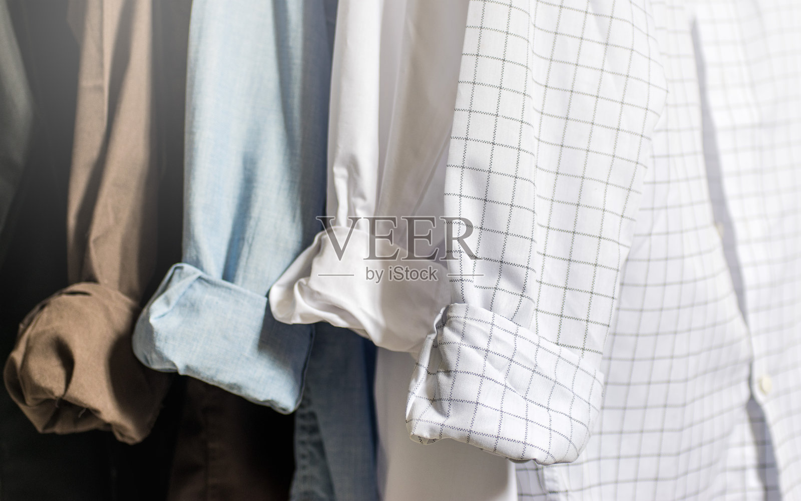 衣柜内部，展示折叠袖口和袖口的男士正装衬衫，白色，蓝色，棕色和黑色衬衫，浅色调和柔和的焦点照片摄影图片