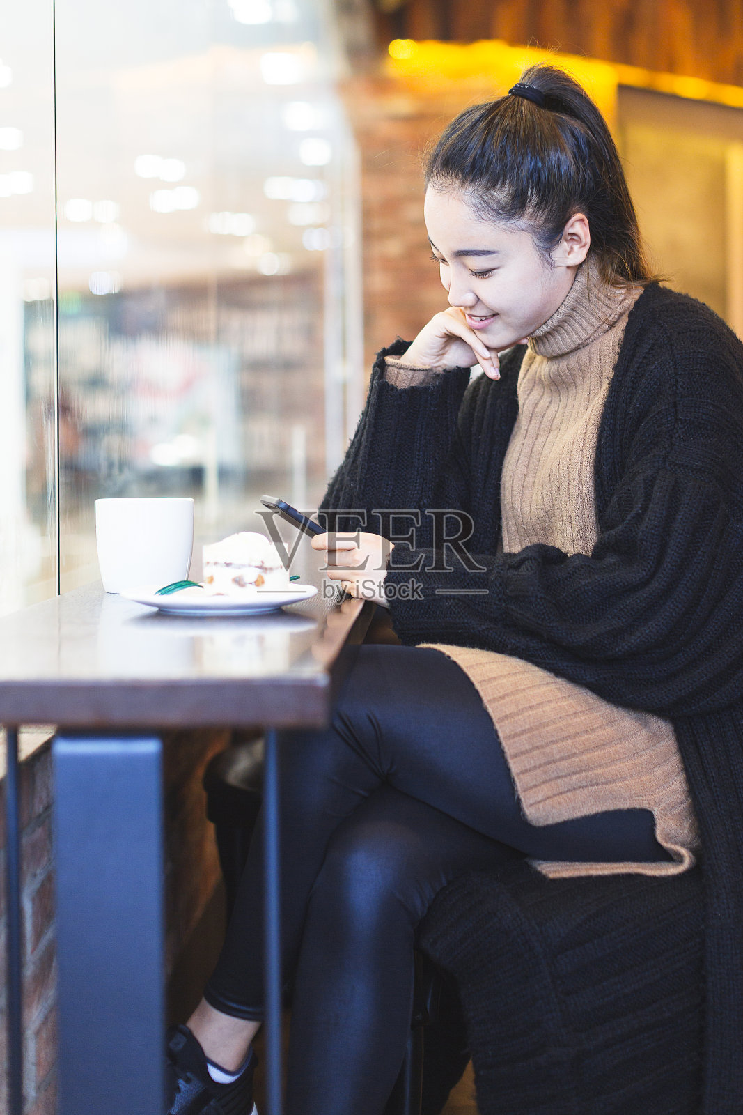 一个女人正在咖啡馆里喝着咖啡吃着糖果，手里拿着手机照片摄影图片
