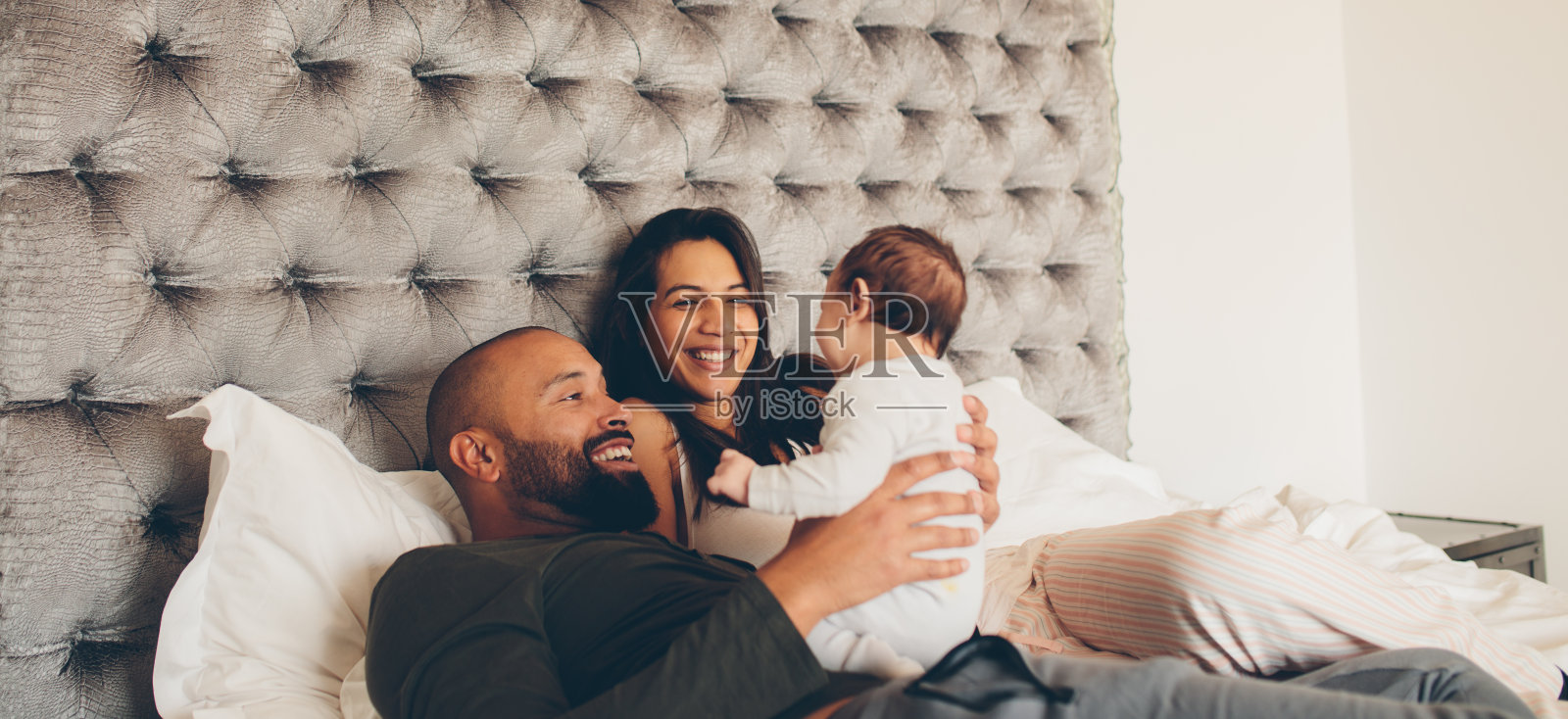 快乐的父母和他们刚出生的儿子在床上玩耍照片摄影图片