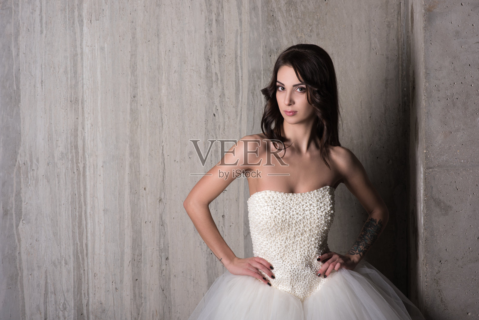 迷人的年轻女子在白色婚纱对着灰色混凝土墙摆姿势照片摄影图片