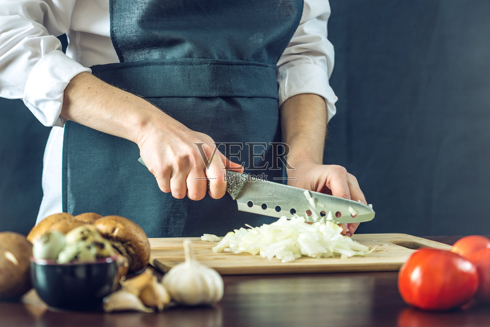 穿黑围裙的厨师用刀切洋葱。环保烹饪产品的概念照片摄影图片
