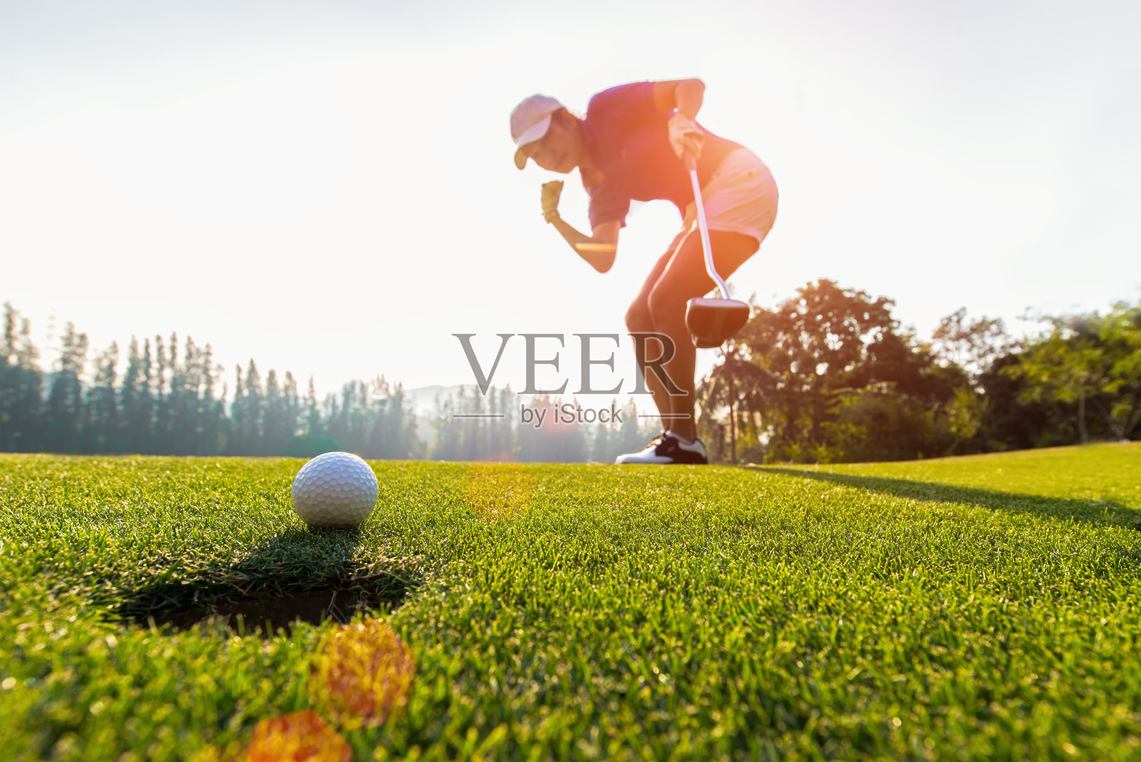 亚洲女子高尔夫球手行动赢后，把高尔夫球在绿色的高尔夫，日落时间，复制空间。健康的概念照片摄影图片