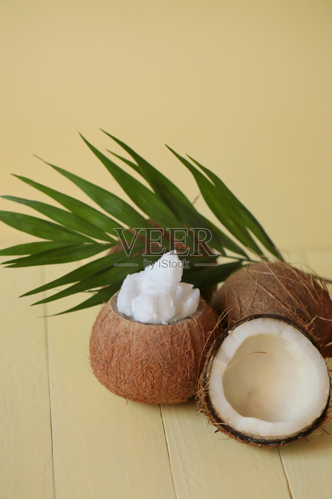 天然椰子油。椰子油片在椰子壳和棕榈叶在黄色木板背景照片摄影图片