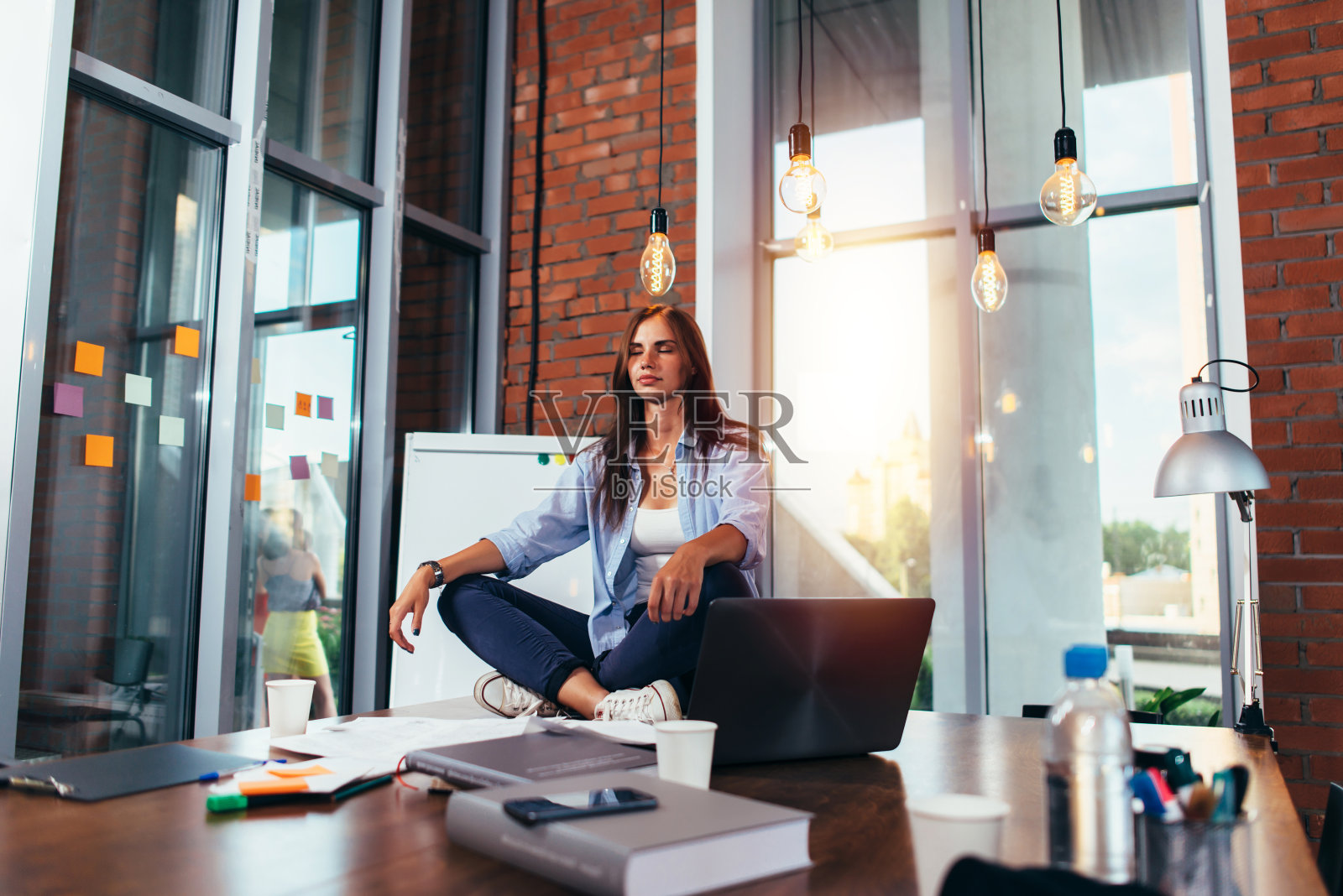 年轻的女商人在她的办公室里坐在工作桌上莲花姿势沉思照片摄影图片