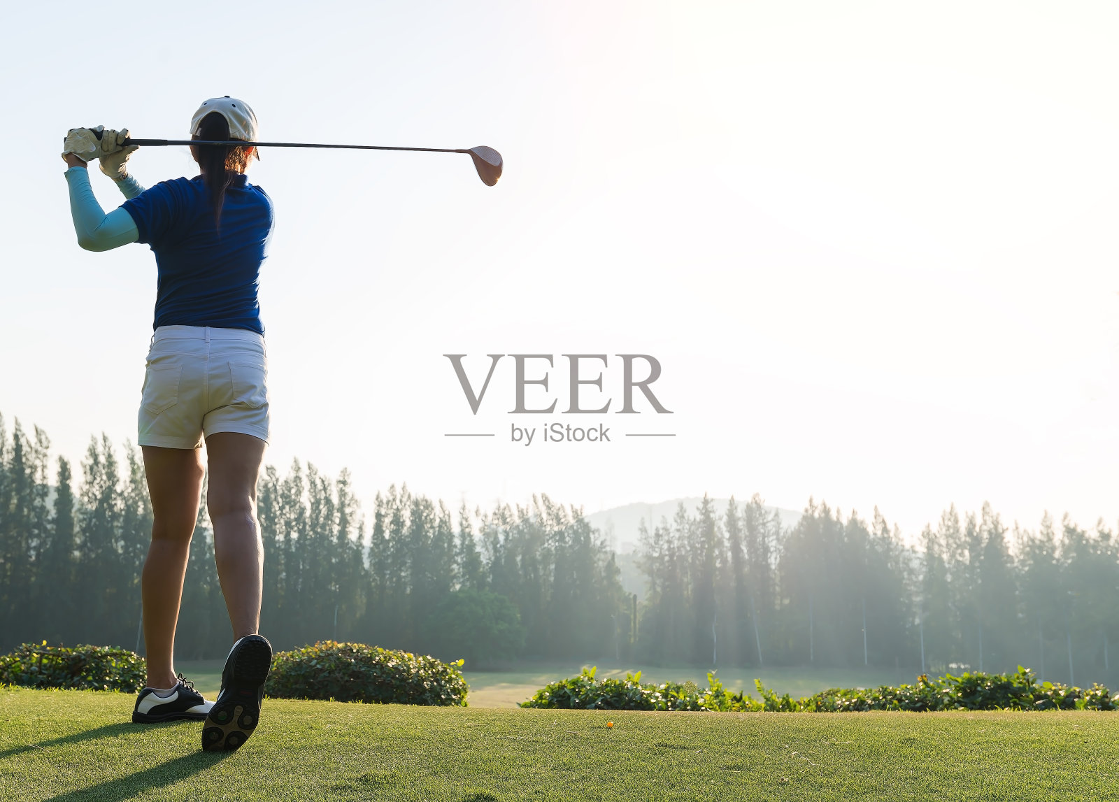 女子高尔夫球手击球的背景风景优美。专注于球。照片摄影图片