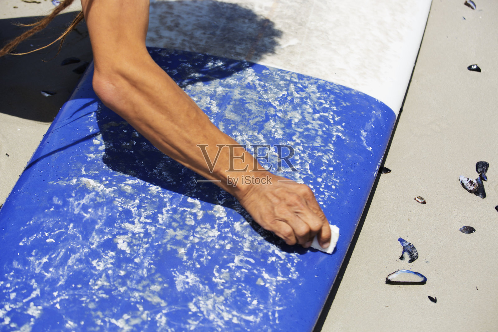 一名男子在海滩上将冲浪蜡涂在冲浪板上照片摄影图片