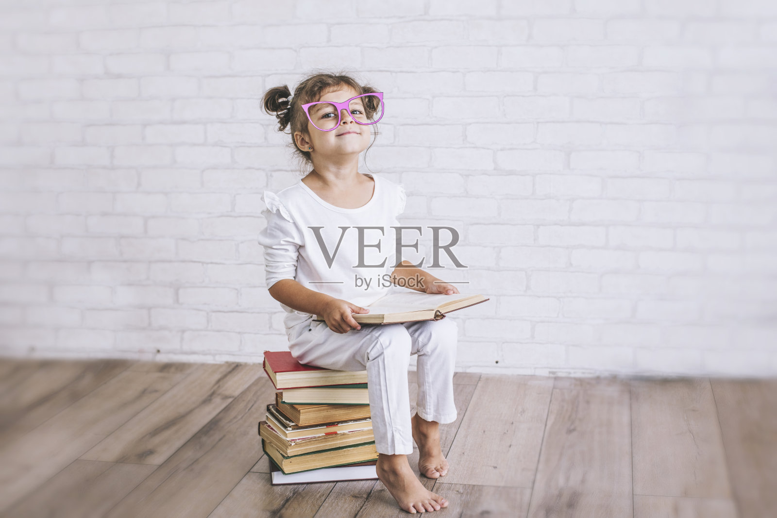 小女孩戴着眼镜坐在一堆书上照片摄影图片