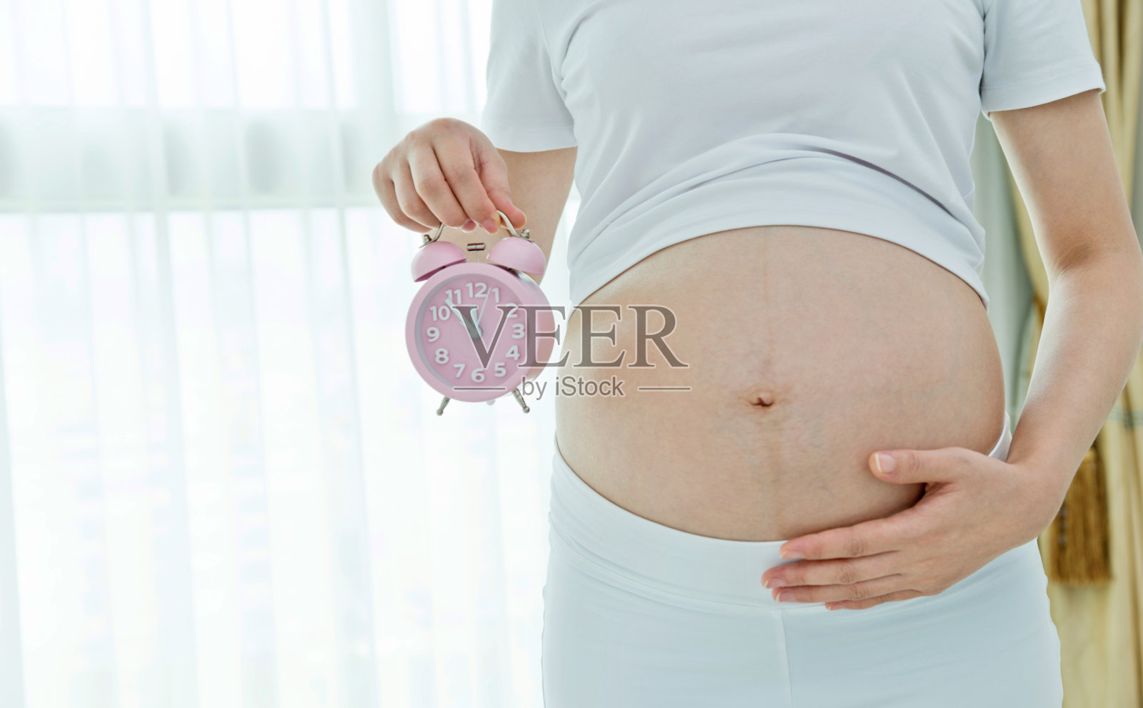 一个孕妇把闹钟放在肚子上照片摄影图片