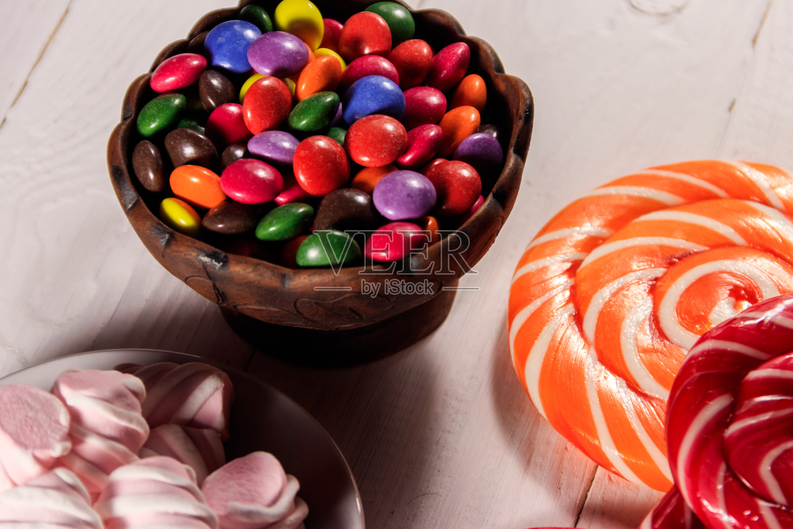 白色木桌上的陶瓷碗里装着五颜六色的纽扣形巧克力糖果照片摄影图片
