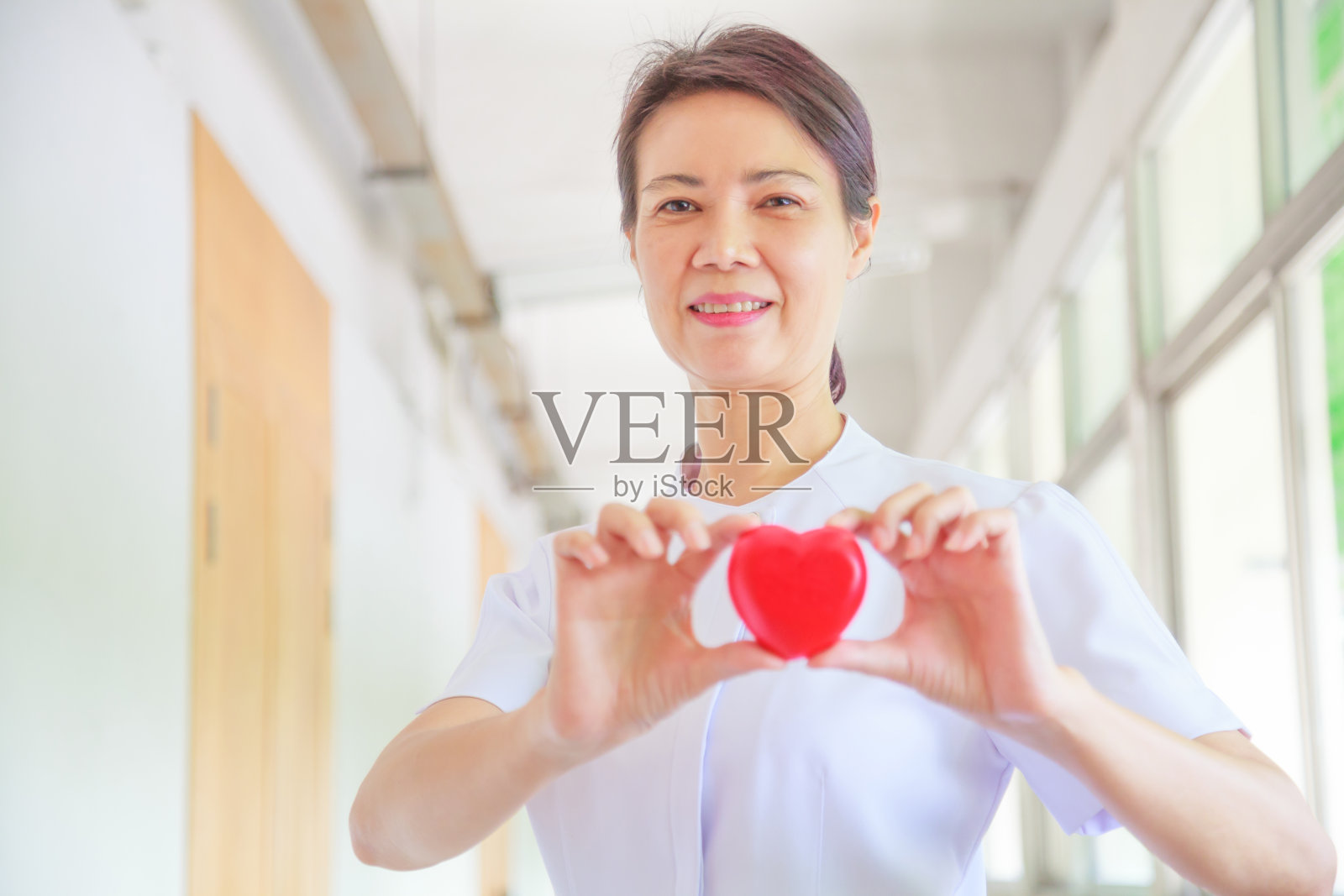 微笑的女护士捧着红色的微笑心在她的手中。红心形状代表对病人高品质的服务精神。专业，专业的白色制服和情人节的概念照片摄影图片